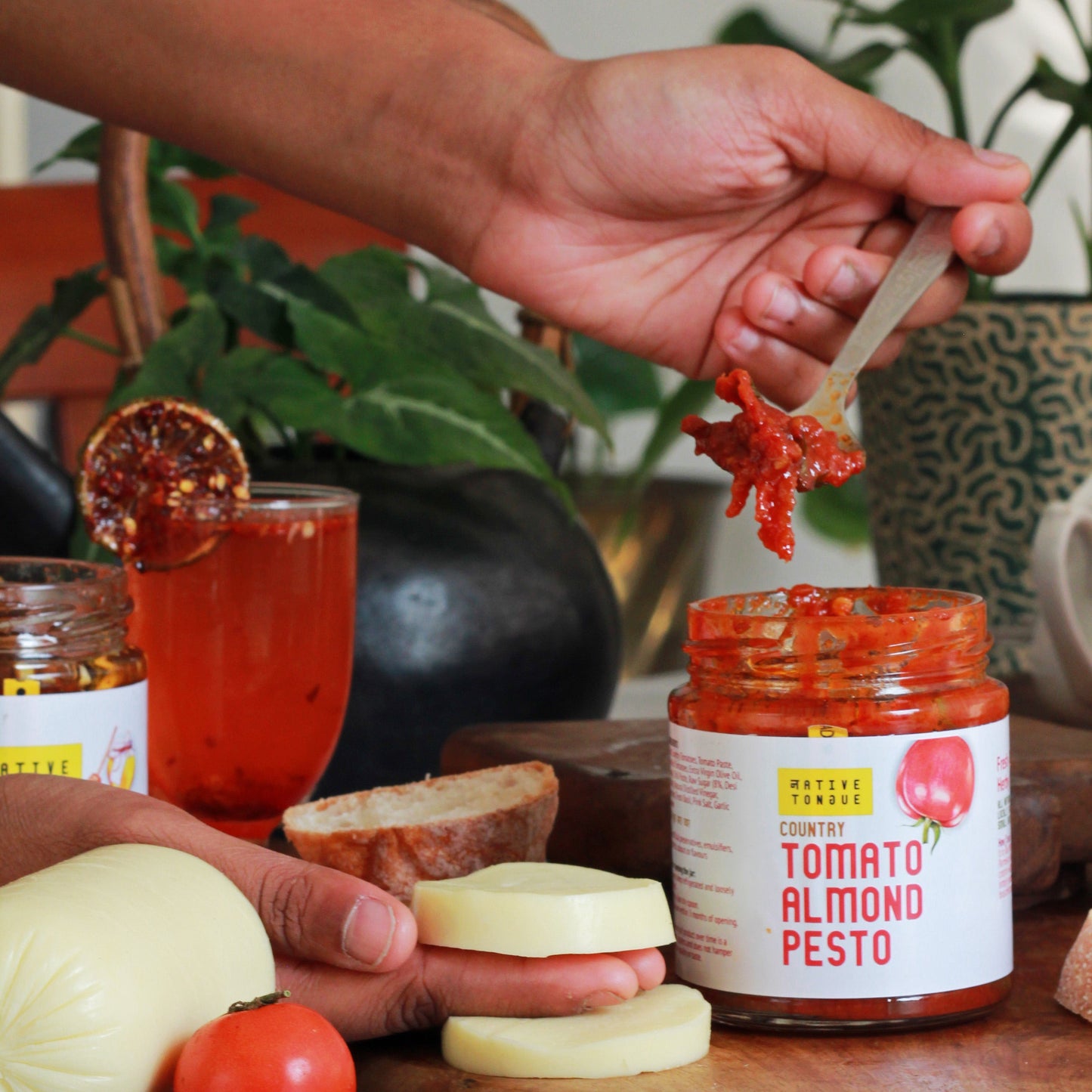 Person preparing food with a jar of Tomato Almond Pesto on a table.