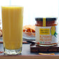 Two glasses of a Mango smoothie next to a jar of 'Alphonso Preserve' on a wooden tray.