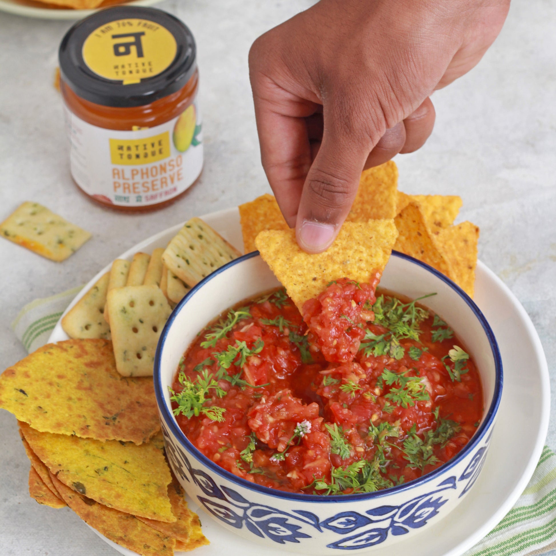 Bowl of salsa with tortilla chips and a jar of salsa on a plate.