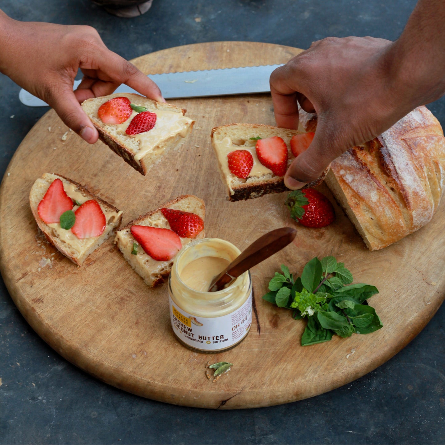 Person preparing strawberry toast on a wooden board with a jar of cream cheese.