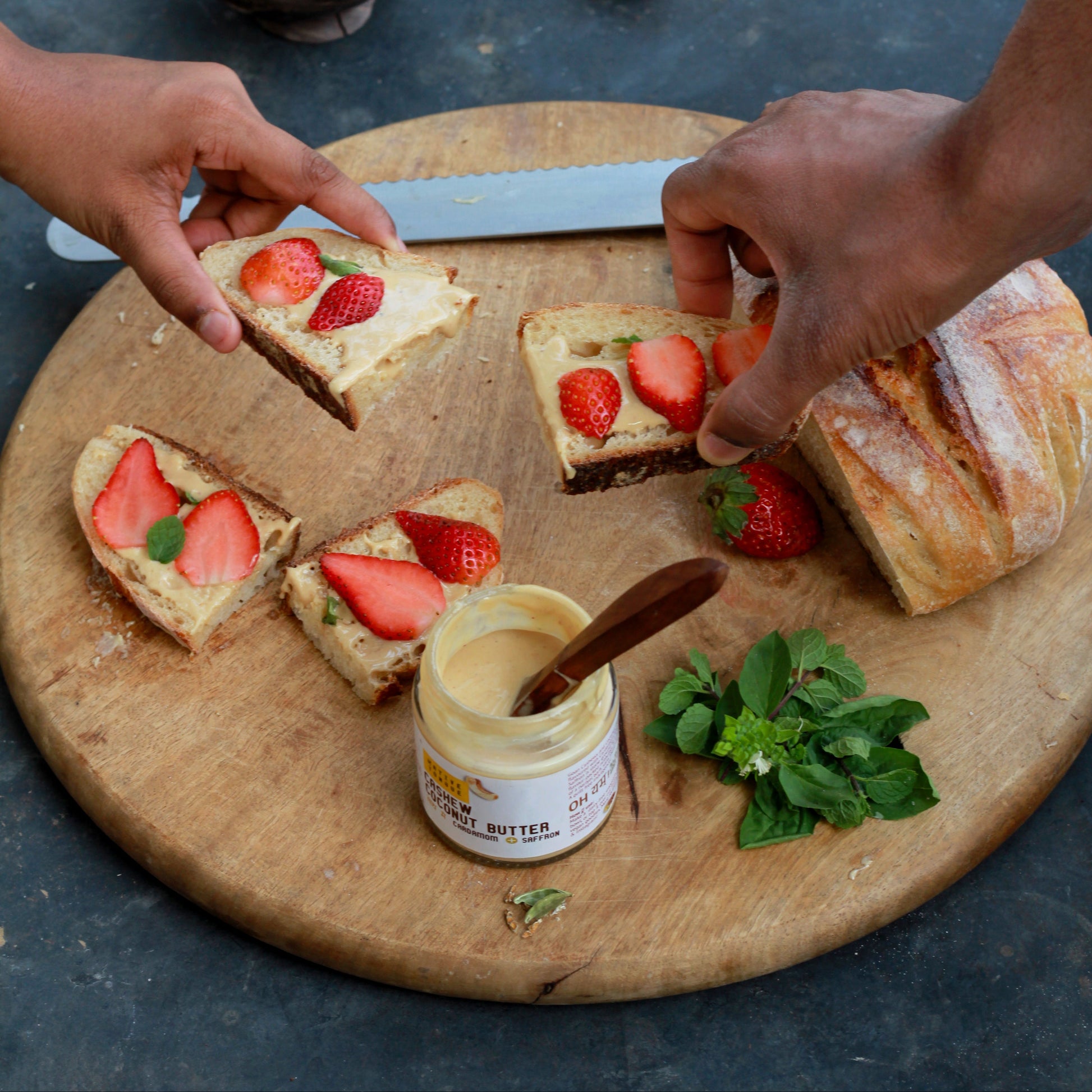 Person preparing strawberry toast on a wooden board with a jar of cream cheese.