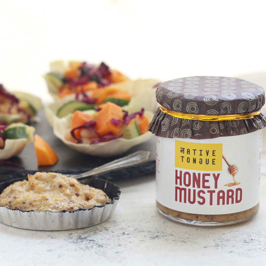 Jar of Native Tongue honey mustard with appetizers in the background