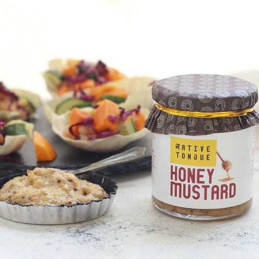 Jar of Native Tongue honey mustard with appetizers in the background
