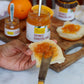 Person spreading orange marmalade on a piece of bread with a jar of marmalade in the background.