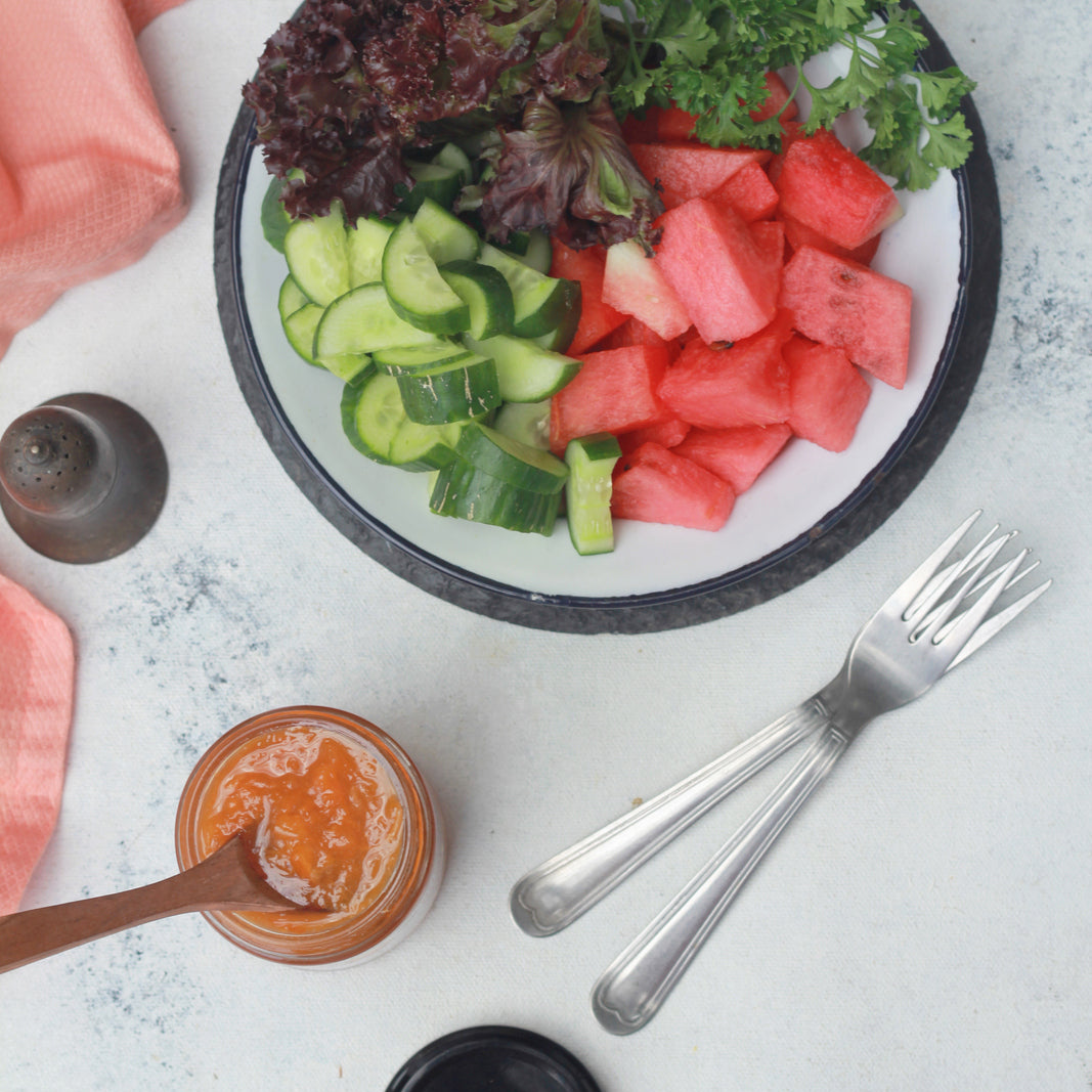 Salad with watermelon, cucumbers, and greens on a plate with a small container of dressing.
