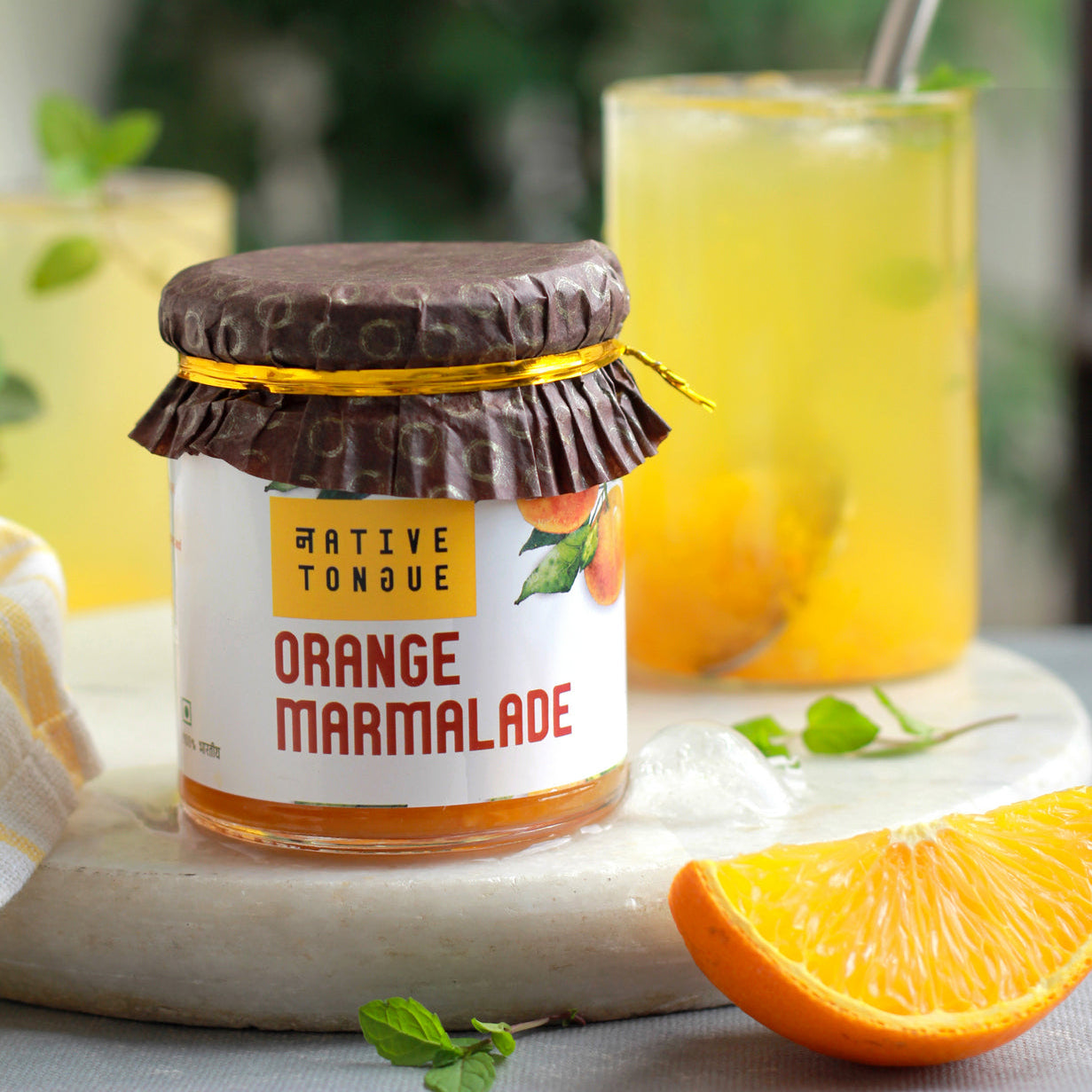 Jar of Native Tongue Orange Marmalade with oranges and a drink in the background