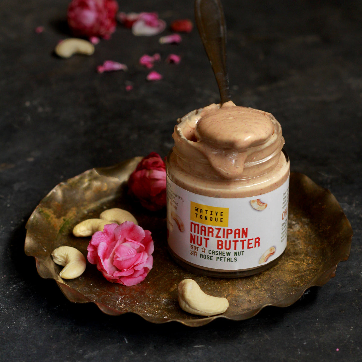 Jar of Marzipan Nut Butter with a spoon on a decorative tray with flowers and nuts.