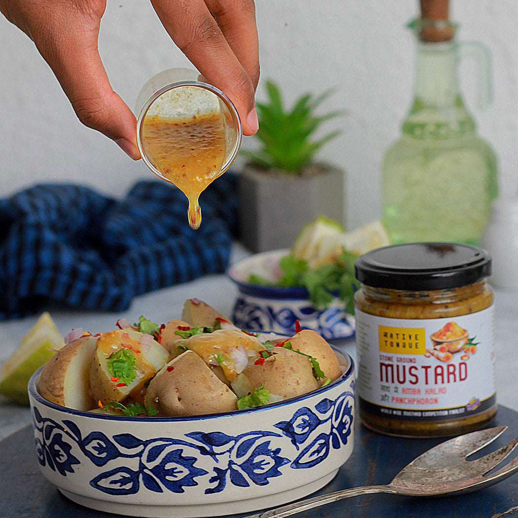 Person pouring mustard over a dish with a jar of mustard on a table.