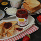 Jar of strawberry preserve on a plate with toast and a strawberry on a dark surface.
